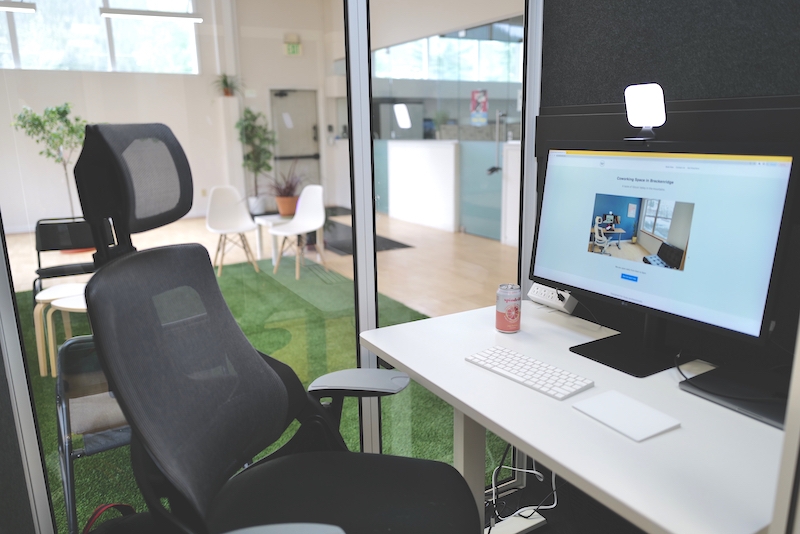 Breckworks Mountain Cabin. An office pod equipped with an external monitor, 4k camera, a vanity Zoom light, a sit-stand desk, and an ergonomic office chair. The pod comes with ventilation and its own lights.